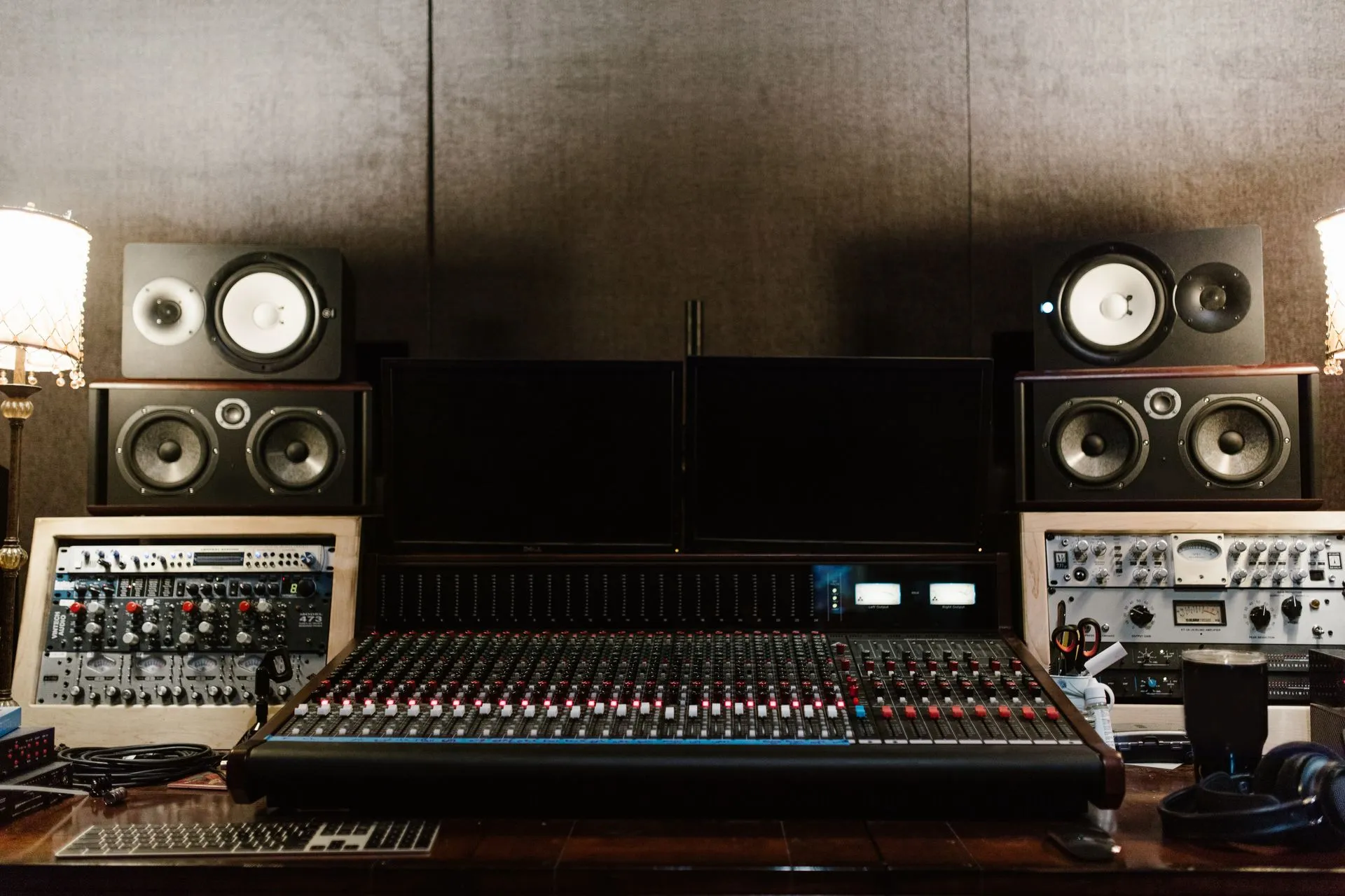 A recording studio mixing console with monitor speakers behind it
